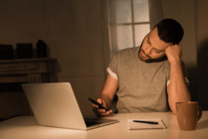 Man at home on laptop looking at phone