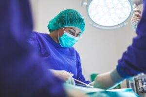 Female surgeon in blue scrubs, mask and hairnet performing operation