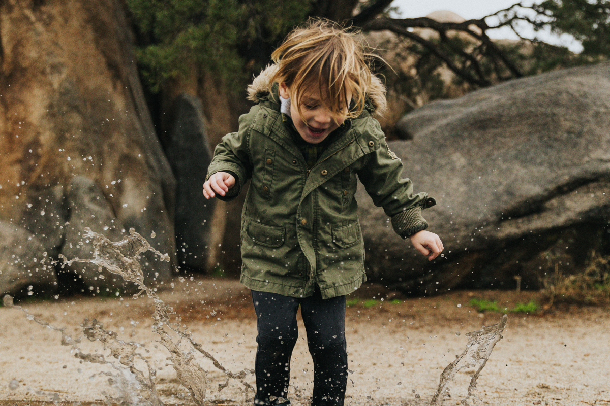 Child in green jacket jumping in a puddle