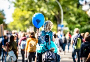 Young girl holding blue balloon with africa outline drawn on it, sitting on man's shoulders walking outdoors through crowd