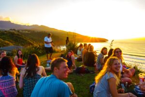 Group of adults socialising on cliff with sea view at sunset in Raglan, New Zealand