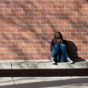 A young girl looking despondent, sits against a brick wall