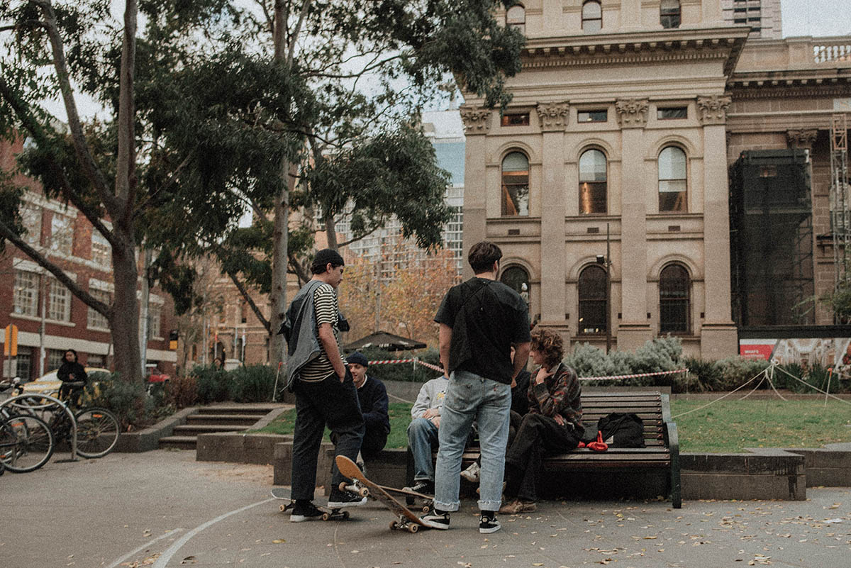 Four young people on a bench, with skateboards, in front of a building. Photo by Kevin Laminto, via Unsplash